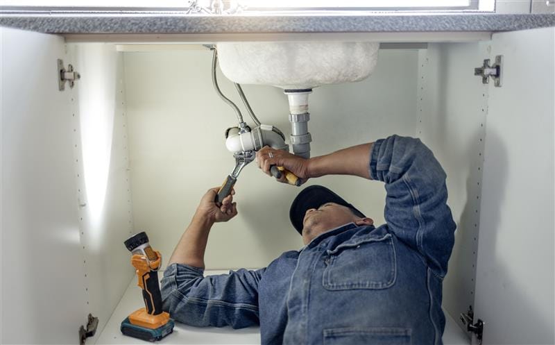 Plumber repairing pipes beneath a bathroom sink in DeLand