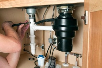 Plumber repairing a garbage disposal beneath a kitchen sink in DeLand