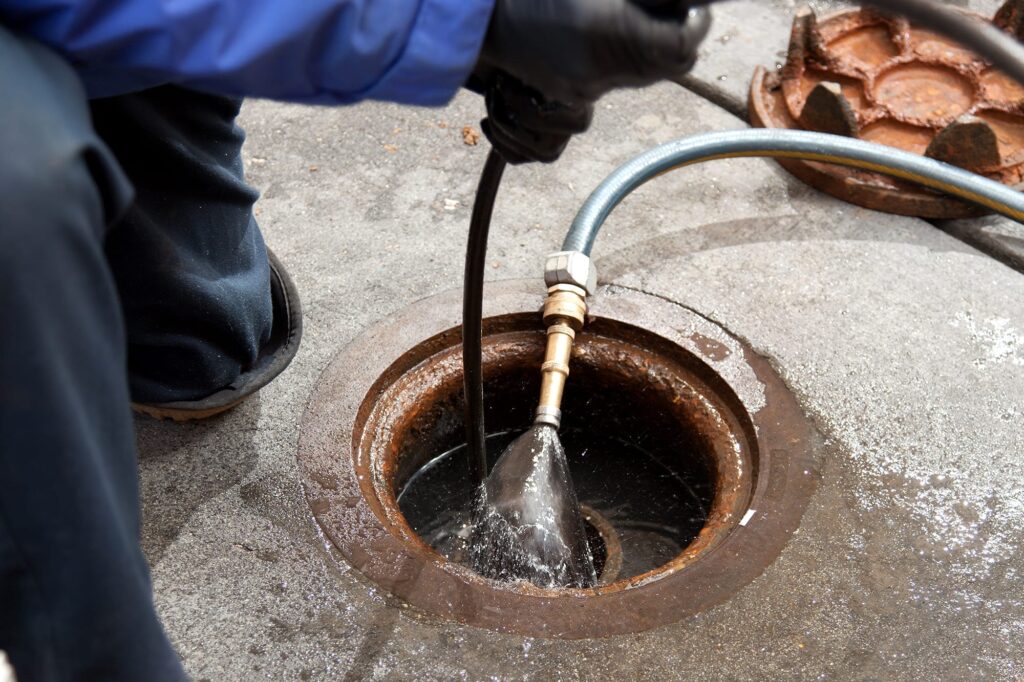 Plumber hydro jetting a sewer line through a manhole in DeLand