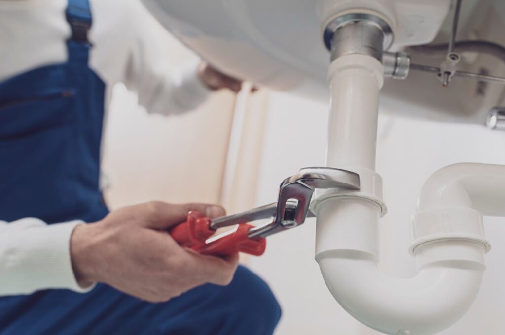 Plumber repairing a white drain pipe beneath a sink in DeLand