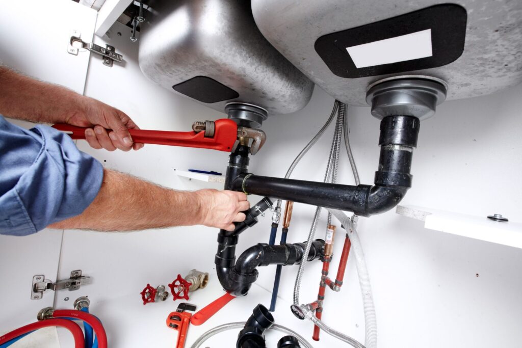 Plumber repairing drain pipes beneath a kitchen sink in DeLand